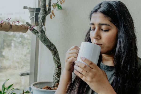 A person calmly drinking tea and looking out a window, practicing everyday mindfulness.